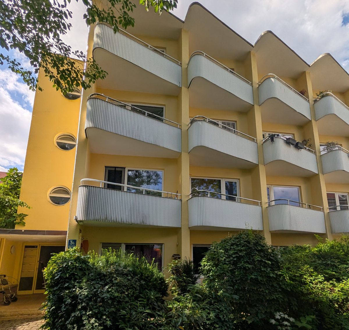 Gelbes Gebäude mit wellenförmigen Balkonen und Hausnummer 3b an der Kaiserstraße in München.
